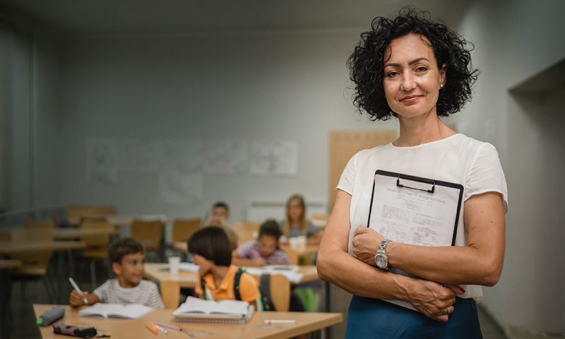 Female school administrator holding a clipboard in a classroom setting