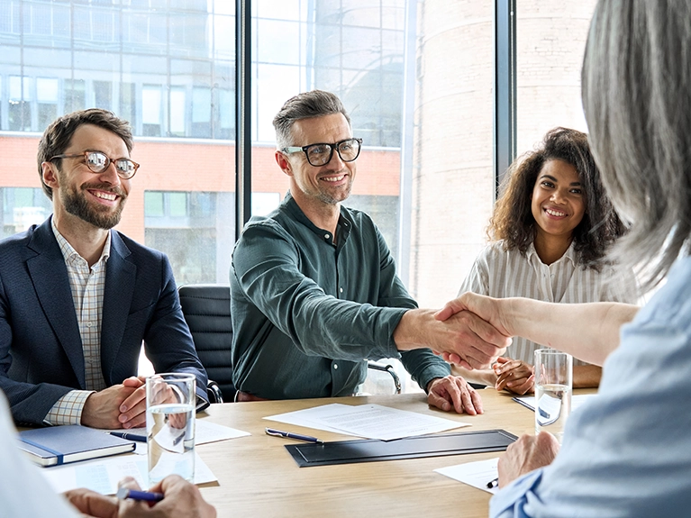 Colegas de trabalho de uma ag&ecirc;ncia de rela&ccedil;&otilde;es p&uacute;blicas conversando e apertando as m&atilde;os em uma mesa