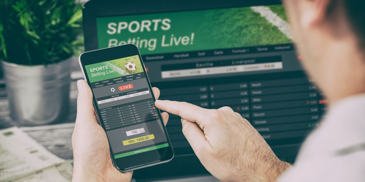 A man places online sports bets using his cellphone and a laptop