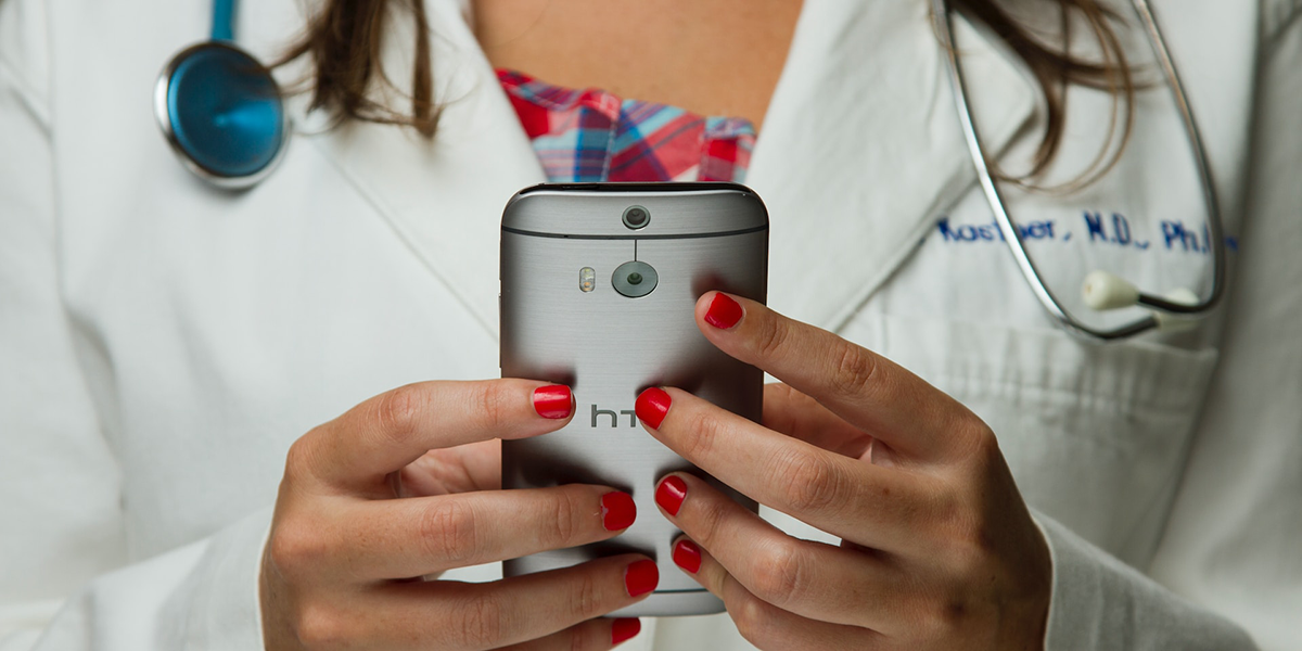 A woman in a doctor's white lab coat handles a cell phone.
