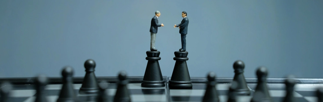 two men in suits standing on chess pieces shaking hands