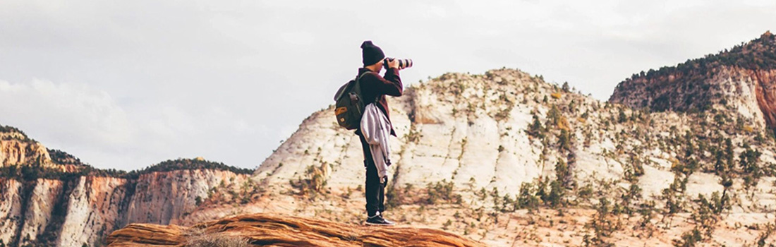 man standing on mountain top taking photographs with large camera